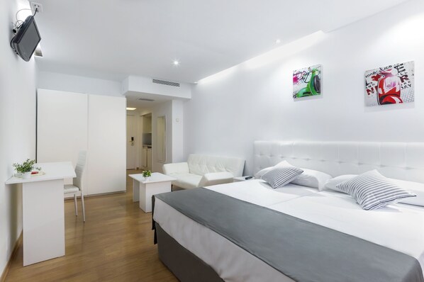 Habitación de hotel moderna con una cama grande, un escritorio y una silla. Hay dos cuadros en la pared y un televisor montado allí.