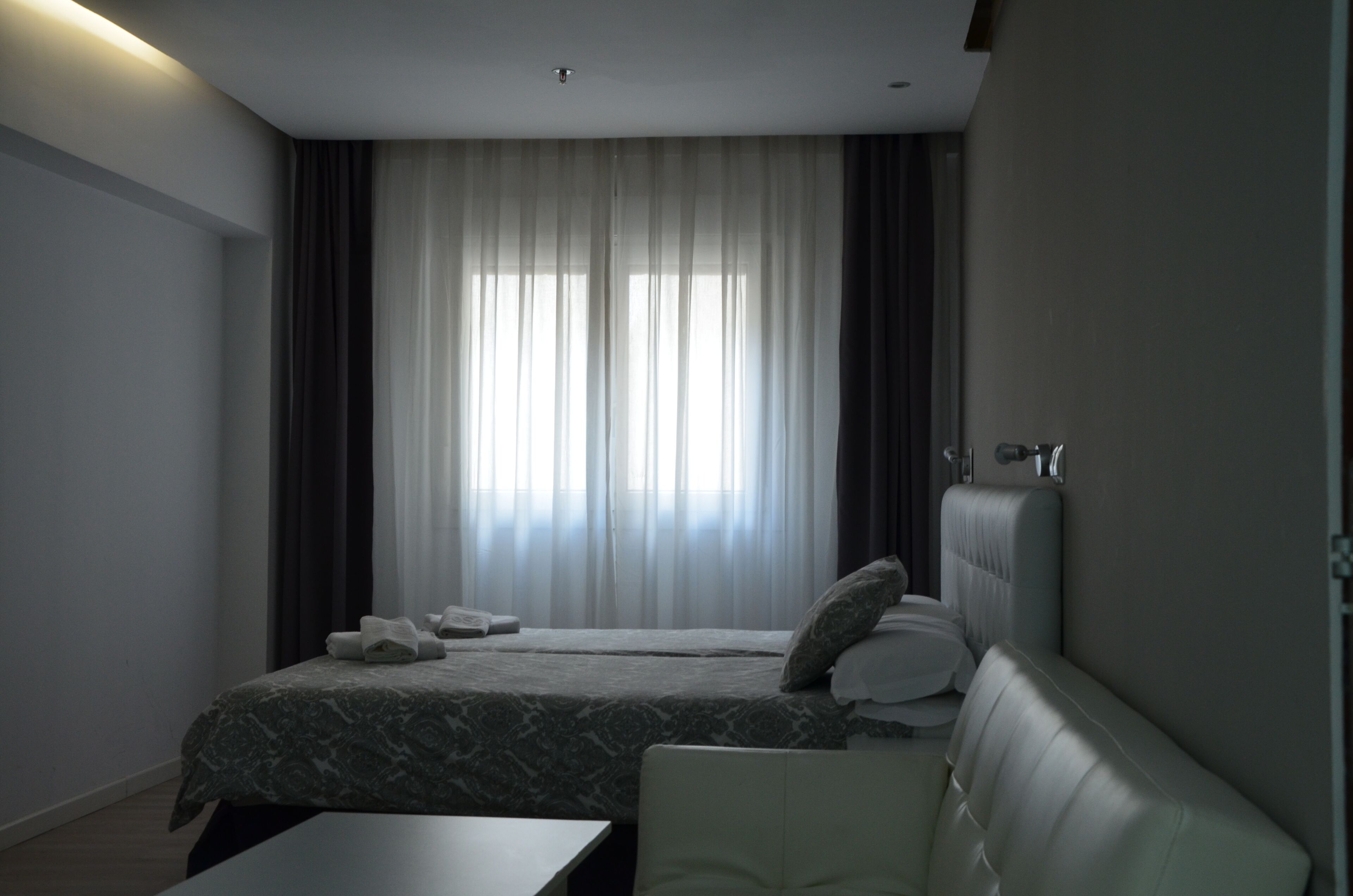 Ein modernes Hotelzimmer mit Bett, Sofa, Schreibtisch und einem Vorhangfenster.