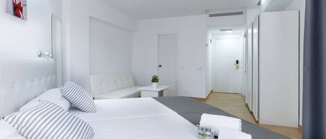 A hotel room with a bed, a small table with a plant, and a hallway leading to a door.
