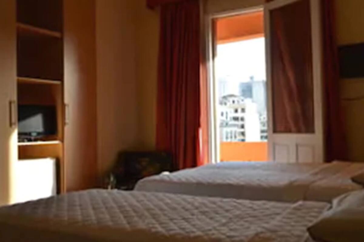 Une chambre d’hôtel avec deux lits, une télévision et une fenêtre avec des rideaux rouges.