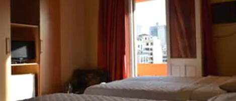 Ein Hotelzimmer mit zwei Betten, einem Fernseher und einem Fenster mit roten Vorhängen.