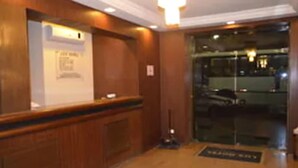 A reception area with a wooden reception desk, a glass door leading outside, and a sign on the wall. - Hotel Lux (São Paulo)