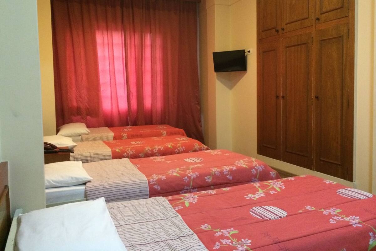 Une chambre avec deux lits, une armoire en bois et un téléviseur fixé au mur.