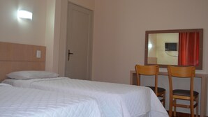 A hotel room with two beds, a wooden headboard, a desk with a chair, and a mirror on the wall. - Hotel Lux (São Paulo)