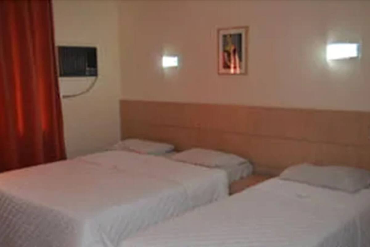 Une chambre d’hôtel avec deux lits simples, une tête de lit, un climatiseur fixé au mur et un tableau encadré.