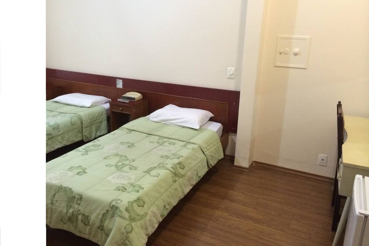 Une chambre d’hôtel avec deux lits simples, des têtes de lit en bois, une petite table de chevet avec un téléphone et un radiateur.