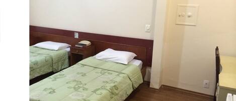 A hotel room with two single beds, wooden headboards, a small bedside table with a telephone, and a radiator.