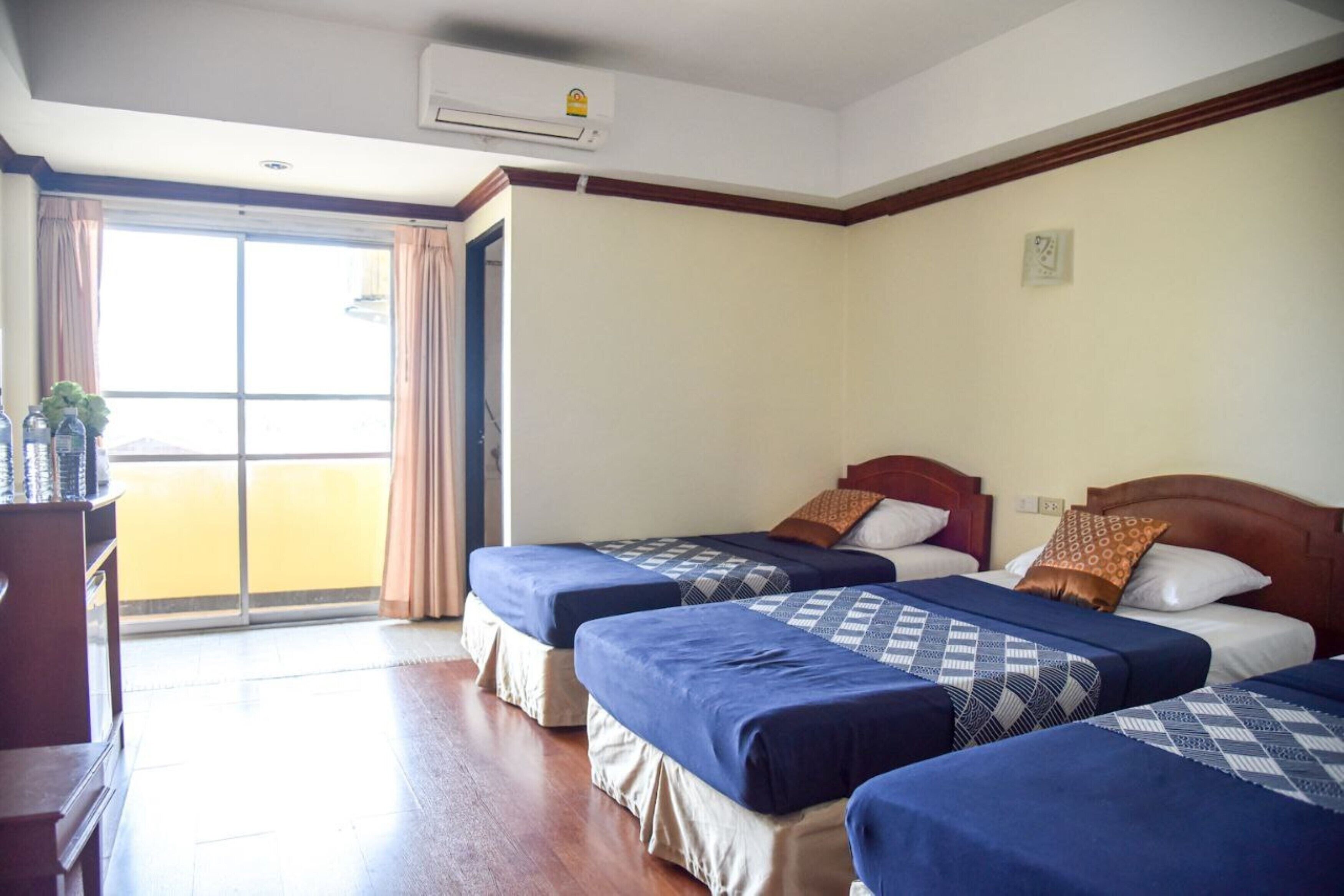 A hotel room with two beds, a wooden headboard, a desk with a plant, and a large window with curtains.