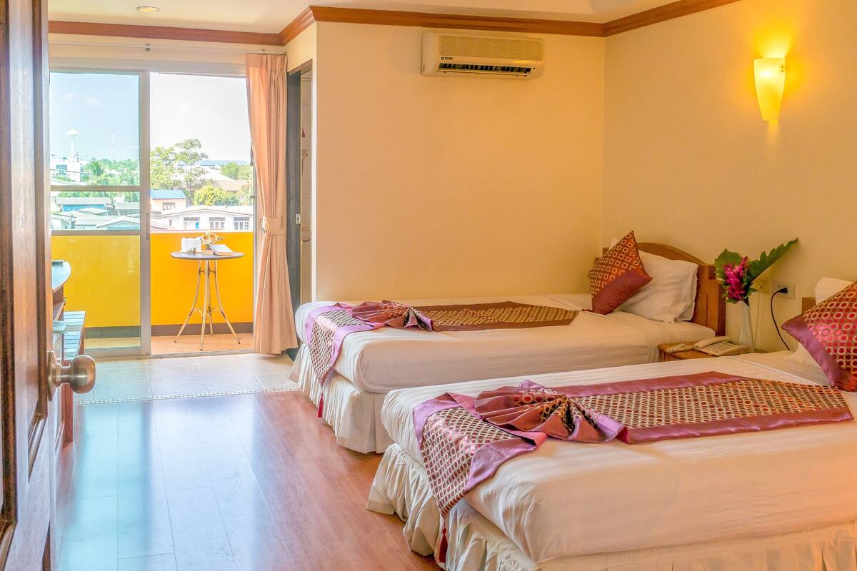 A hotel room with two beds, a balcony, and a view of the cityscape.