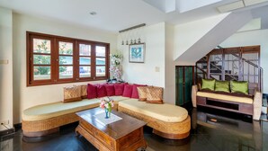 A spacious living area with a large window, a sofa, a coffee table, and a staircase. - Chomsin Hua Hin (Hua Hin)