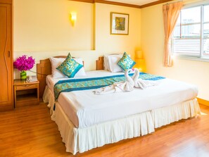 A neatly made bed with a decorative swan towel arrangement, a vase of flowers, and a framed picture on the wall. - Chomsin Hua Hin (Hua Hin)