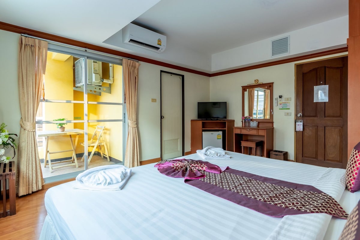 A hotel room with a bed, a desk, a television, and a sliding glass door leading to a balcony.