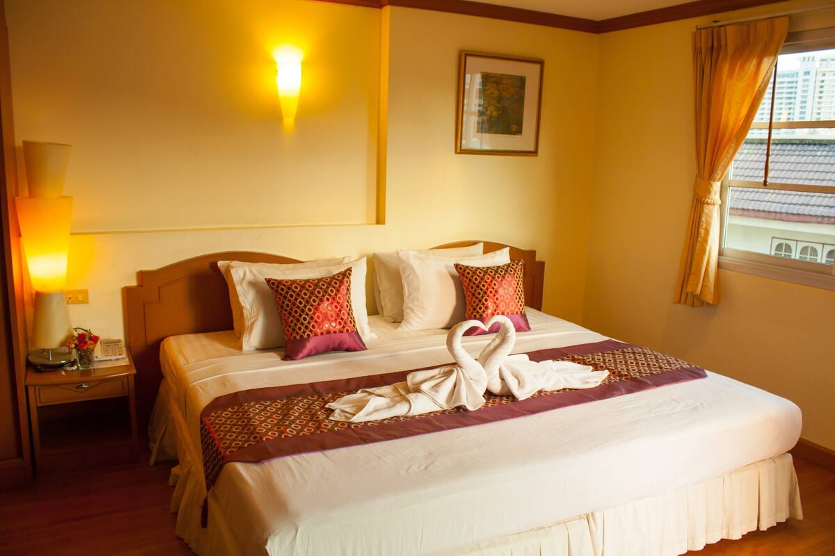 A hotel room with a neatly made bed, a bedside lamp, a framed picture on the wall, and a window with curtains.