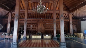 A traditional wooden hall with a chandelier, ornate pillars, and a patterned floor.