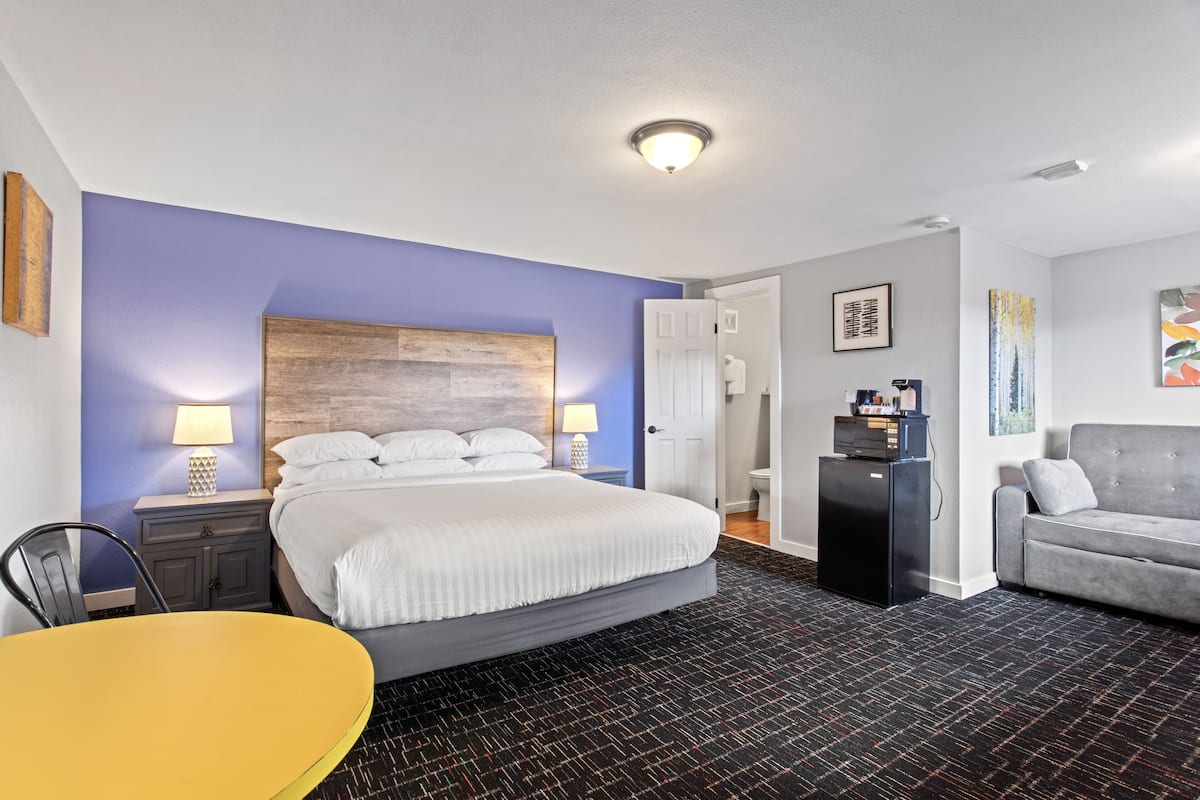 Una habitación de hotel con cama, escritorio, sillón, sofá y una pequeña kitchenette.