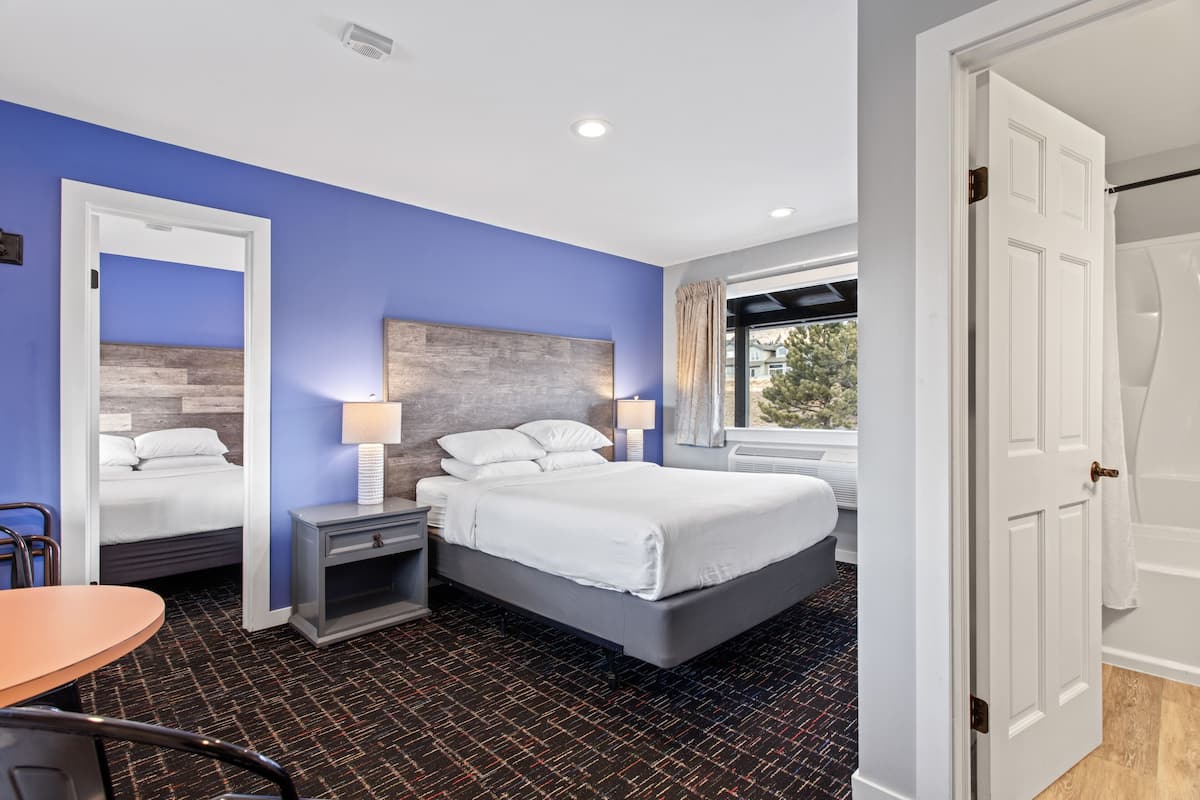 Una habitación de hotel con una cama grande, una mesita de noche con lámpara, una silla y una ventana con cortinas.