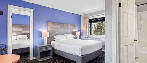 Ein Hotelzimmer mit einem großen Bett, einem Nachttisch mit Lampe, einem Sessel und einem Fenster mit Vorhängen.