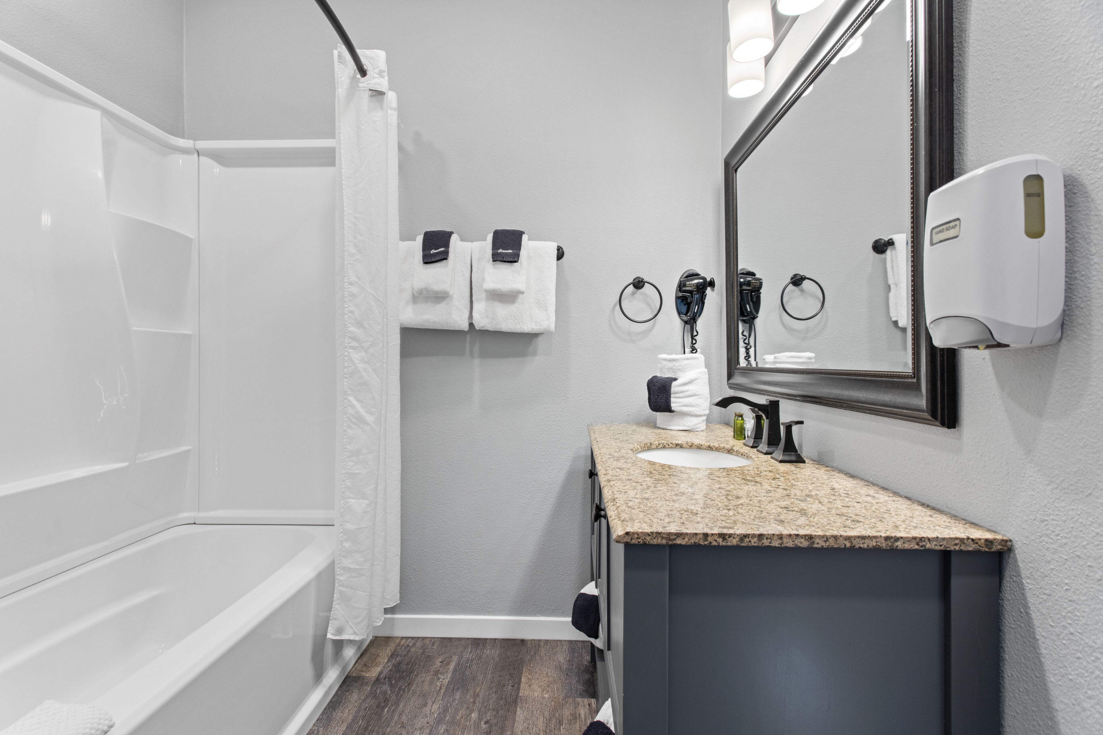 A modern bathroom with a bathtub, a sink with a granite countertop, a mirror, and a hand dryer.