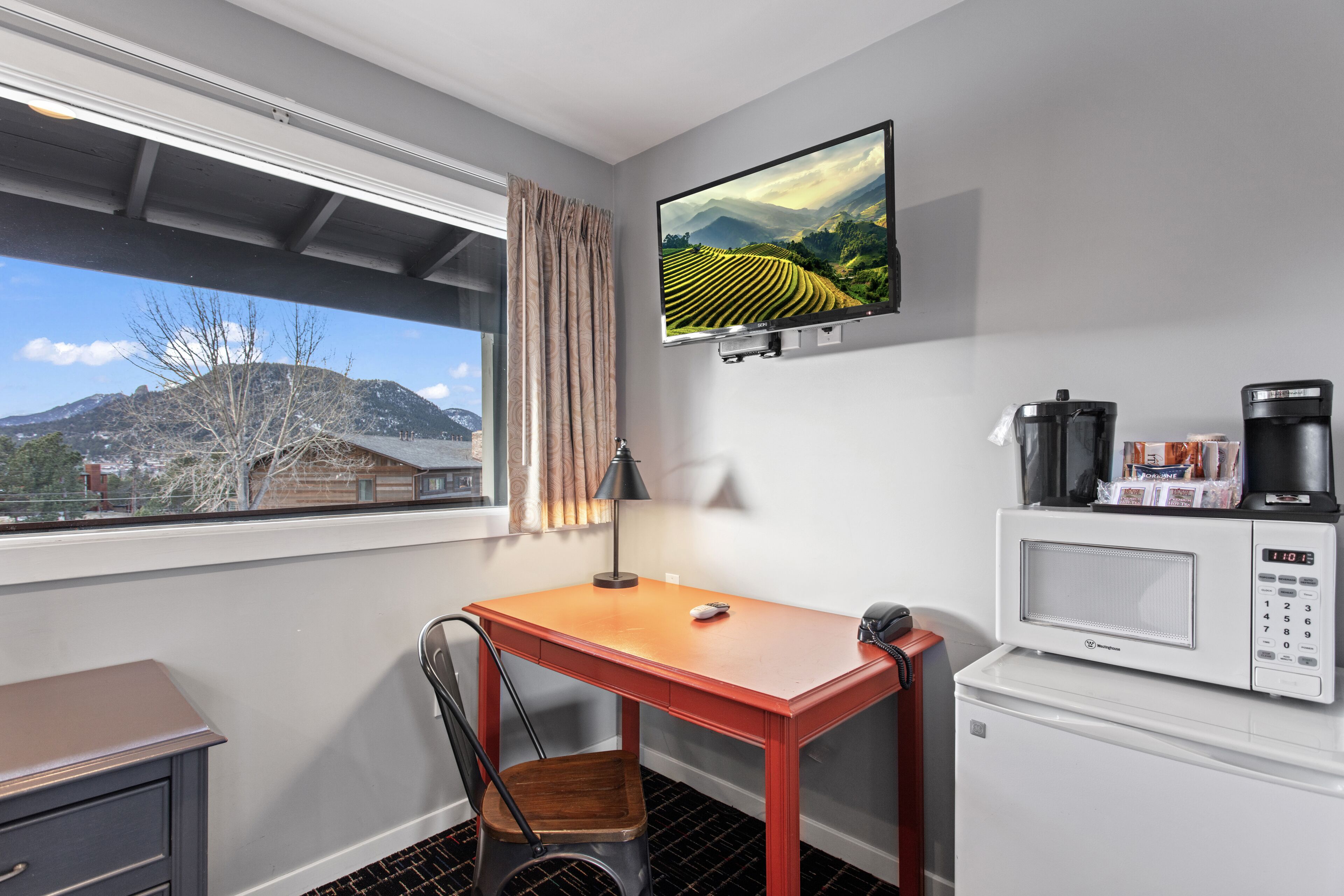 Ein Hotelzimmer mit Schreibtisch, Stuhl, Fernseher, Mikrowelle und Kaffeemaschine.