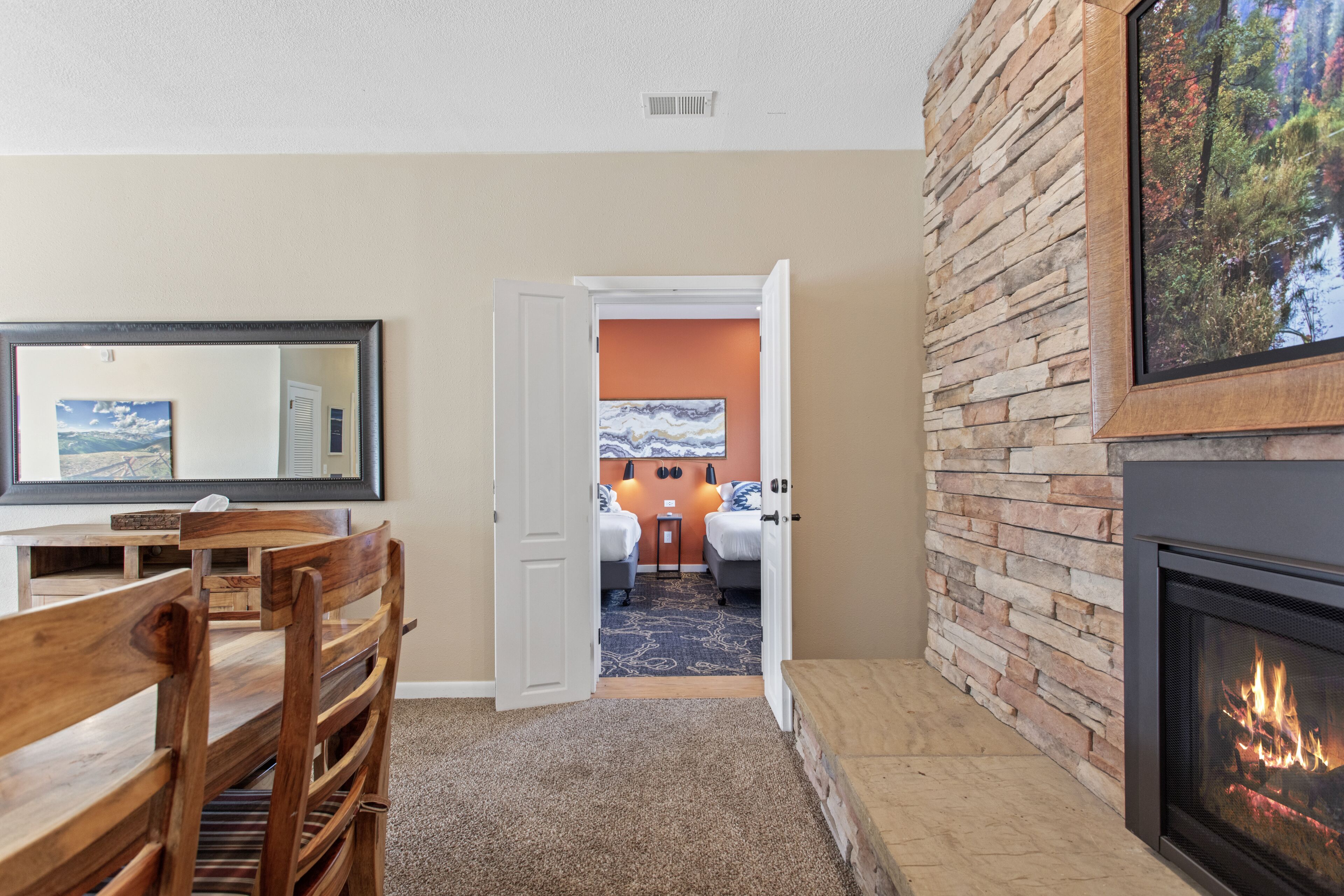 A room with a fireplace, a dining area with wooden furniture, and a view into a bedroom with a bed and a nightstand.