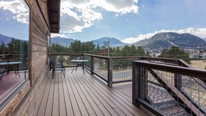 Una terraza de madera con mesas y sillas, con vista a un paisaje montañoso.