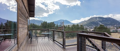 A wooden deck with tables and chairs, overlooking a mountainous landscape.