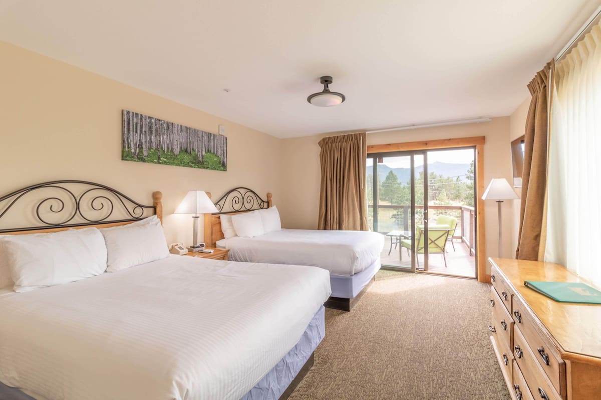 Habitación de hotel con dos camas, un balcón con mesa y sillas, y un cuadro en la pared.
