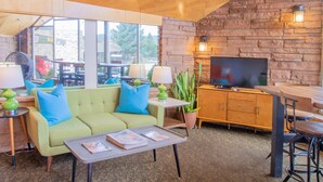 Una sala de estar acogedora con un sofá verde, una mesa de centro con revistas, un televisor y una pared de piedra.