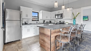Una cocina moderna con armarios blancos, electrodomésticos de acero inoxidable, una isla de madera y taburetes de bar.