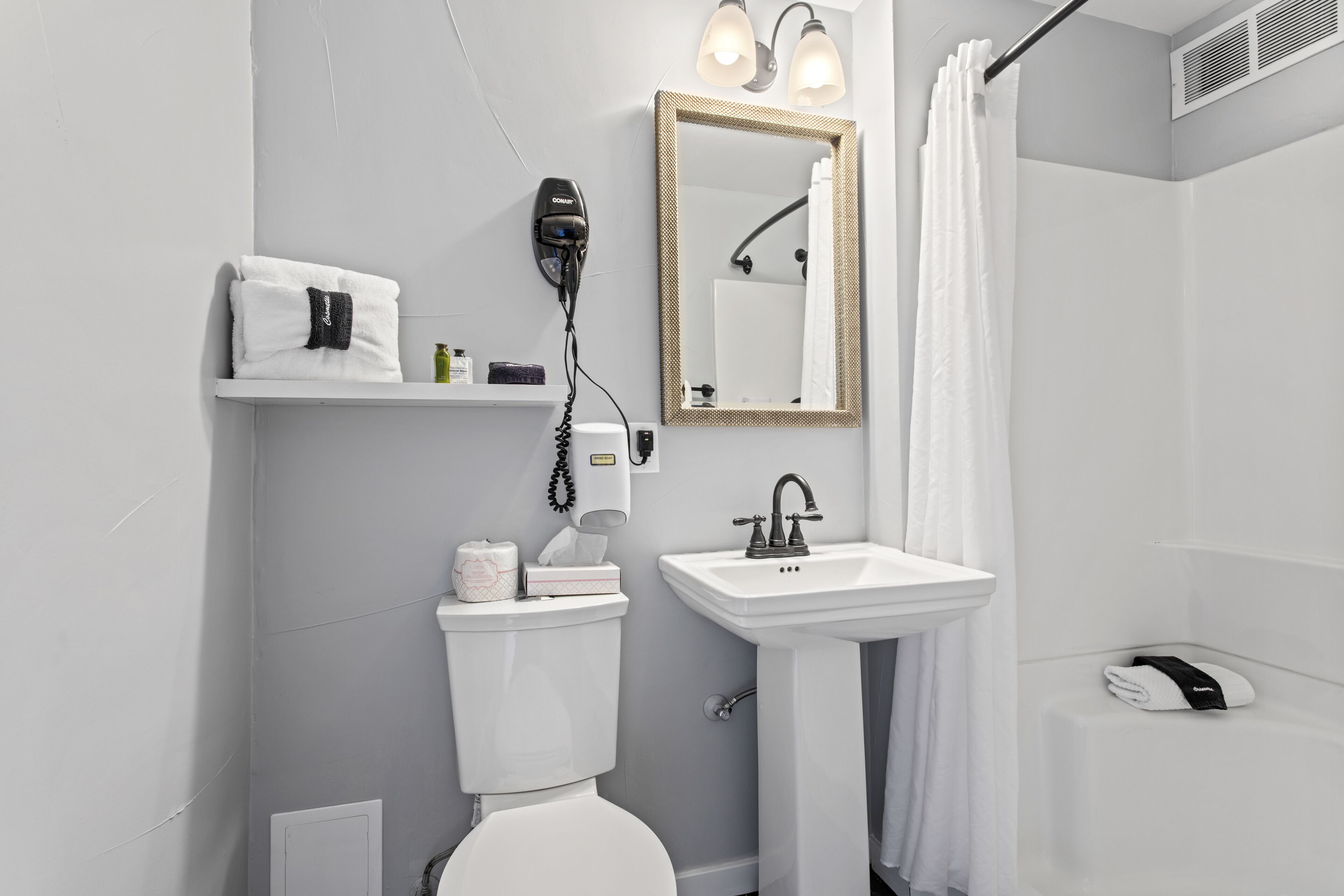 A modern bathroom with a white toilet, a sink, a hairdryer, and a mirror.
