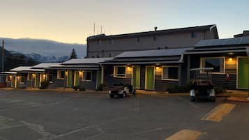 Une rangée de chalets en rondins, avec une chaîne de montagnes en arrière-plan, chacun doté d’un porche et d’une seule étage.