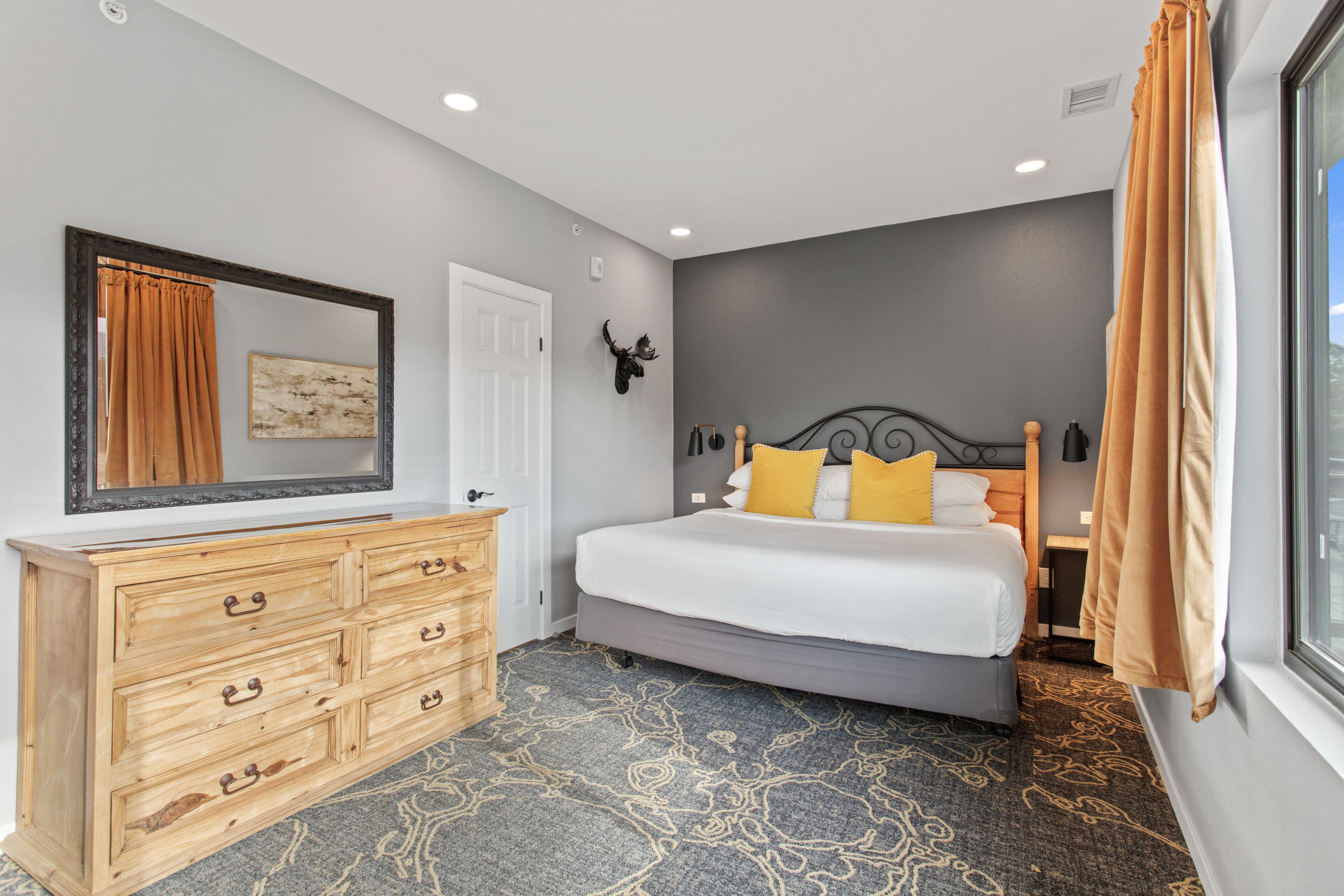 Een slaapkamer met een bed, een houten dressoir en een grote spiegel.