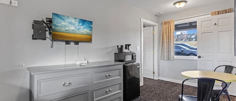 Een compacte hotelkamer met een kitchenette, een eethoek met tafel en stoelen, een aan de muur bevestigde televisie en een deur naar een buitenruimte.