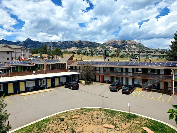 A motel with solar panels, a parking lot, and a mountainous backdrop.