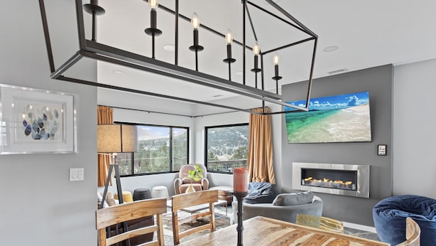 Una sala de estar moderna con una mesa de comedor de madera, una chimenea, un televisor grande y vistas a una playa a través del ventanal.