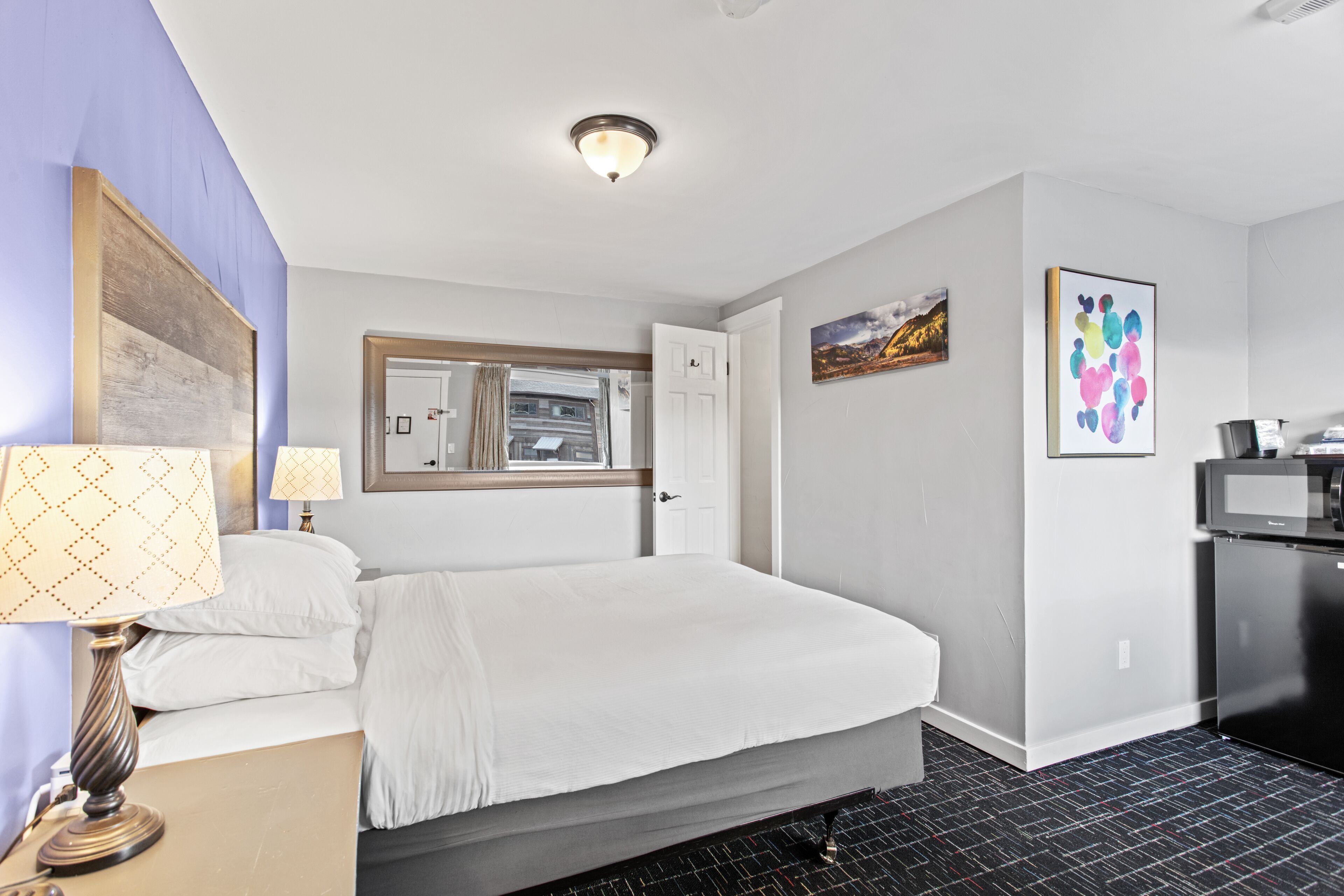 Une chambre d’hôtel avec un lit, un bureau avec une lampe, un réfrigérateur et une fenêtre donnant sur un beau paysage.