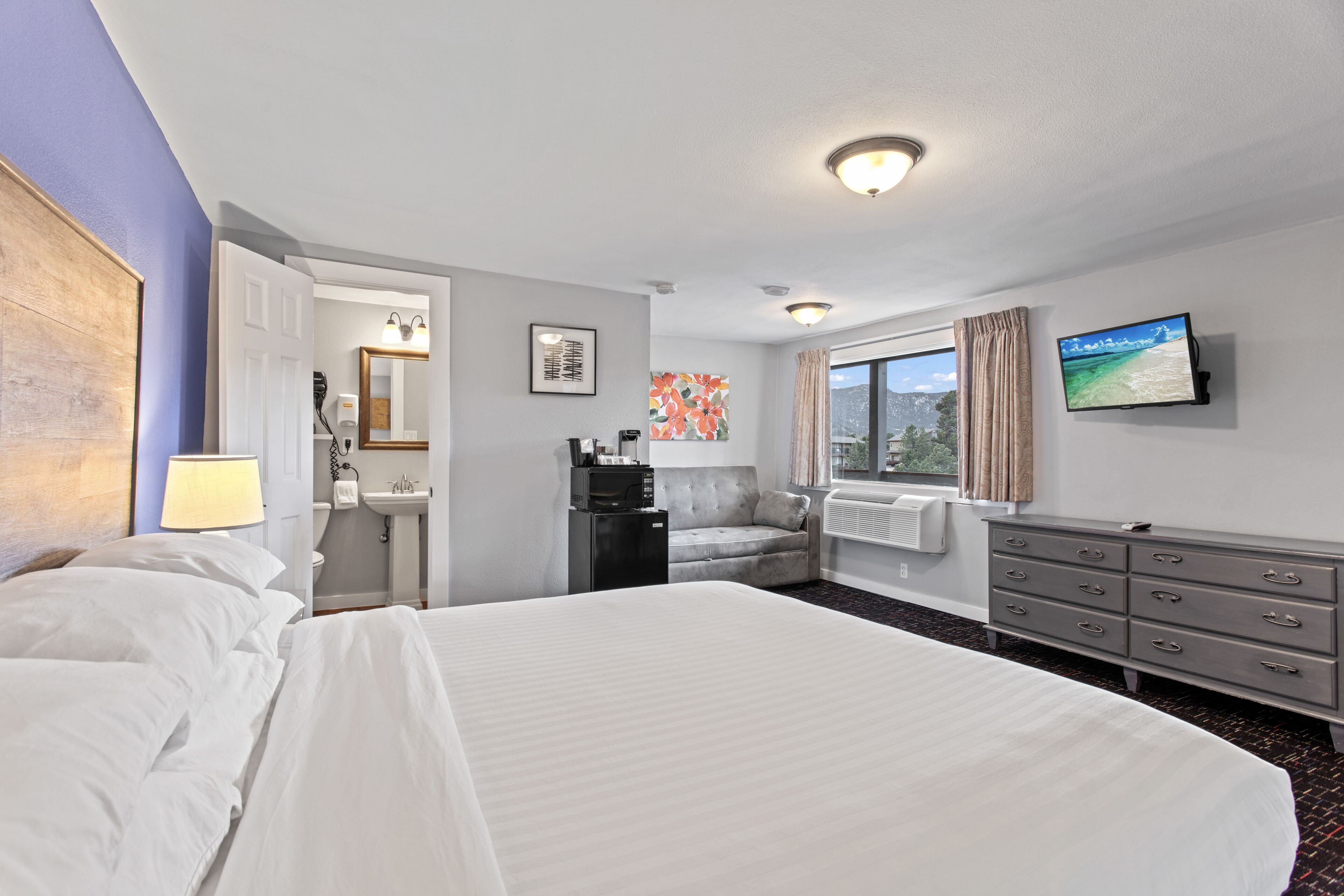 Quarto de hotel com uma cama grande, uma escrivaninha com cadeira, televisão e janela com cortinas.