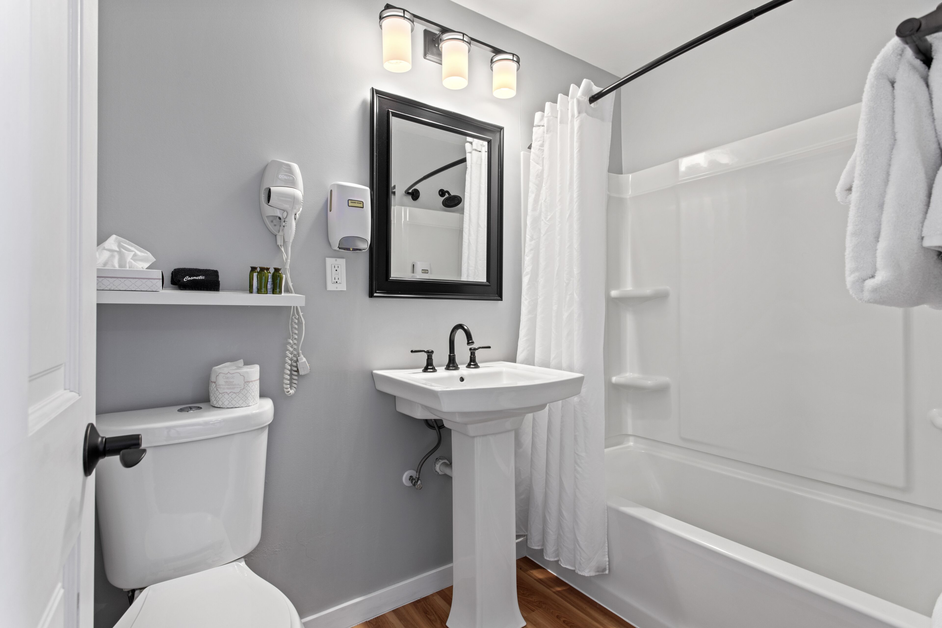 A modern bathroom with a white toilet, pedestal sink, and a shower with a curtain.