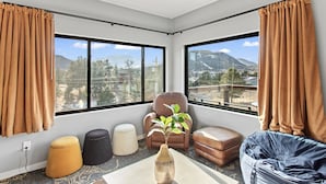 Una sala de estar moderna con un amplio ventanal que ofrece vistas a la montaña, un sillón de cuero, otomanas y un florero con una planta.