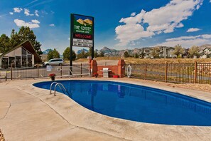 A pool area with a sign for The Coyote Mountain Lodge, a fenced pool, and a building with a sloped roof.