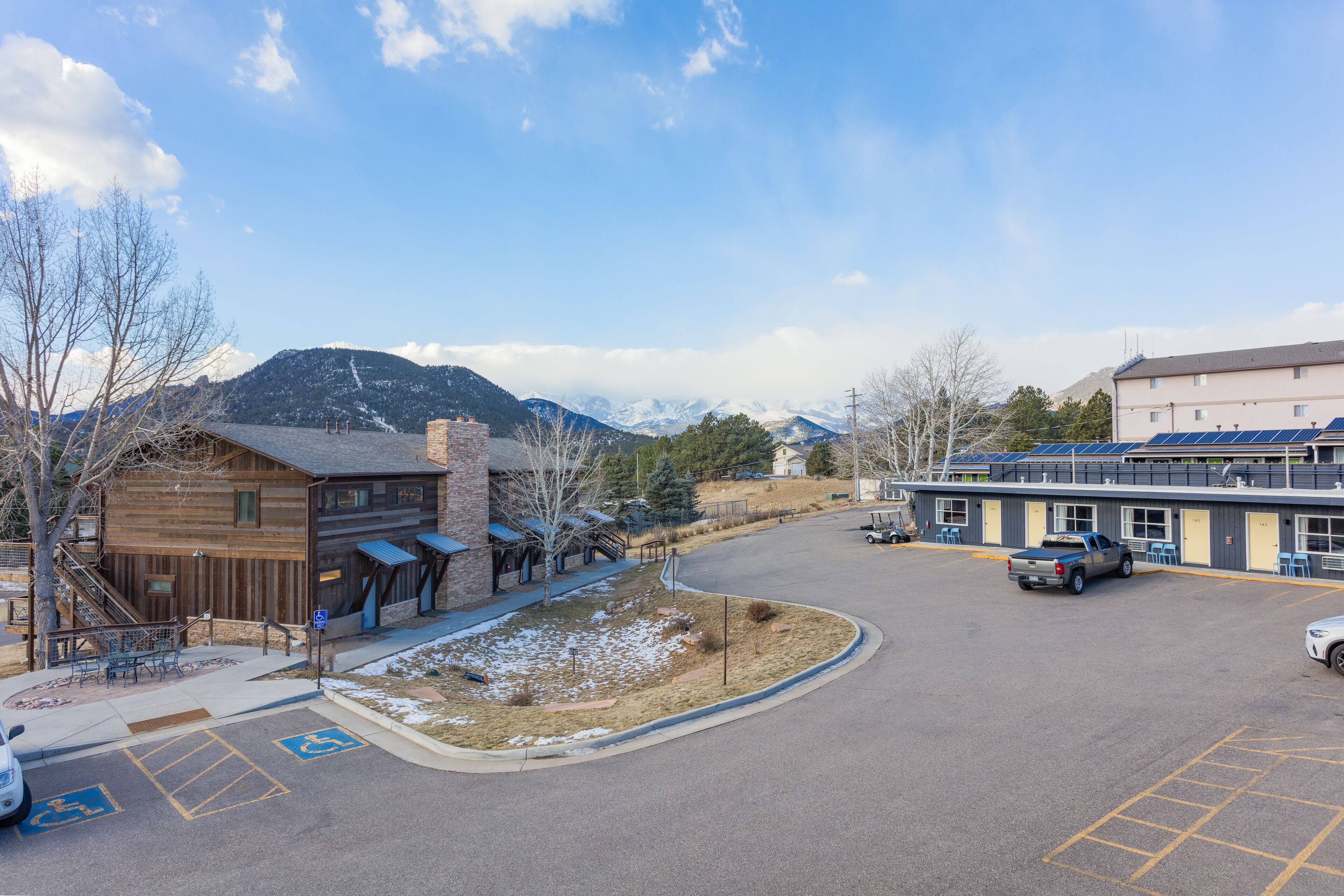 Un parking avec un bâtiment, une montagne en arrière-plan et un ciel dégagé.