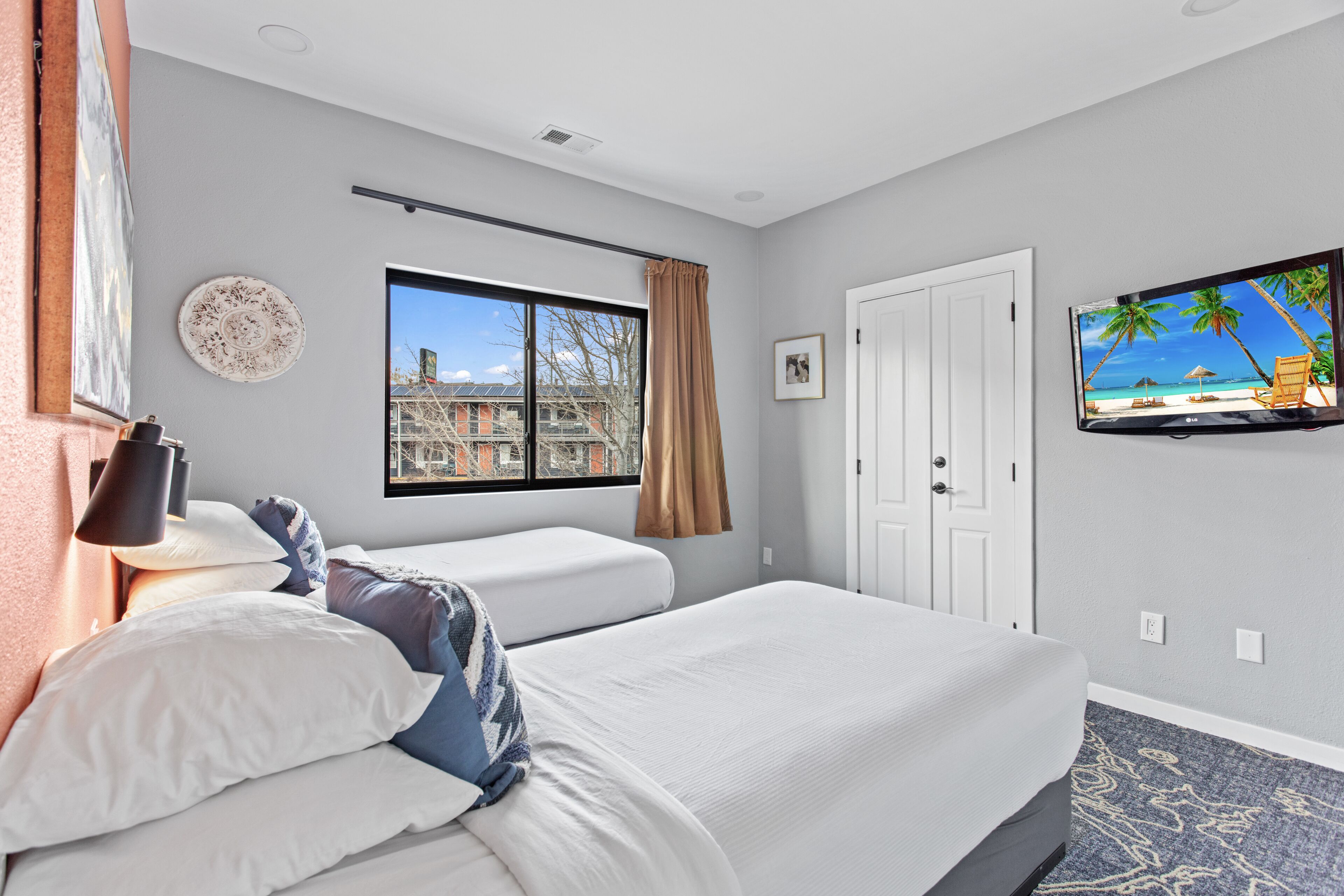 Hotelkamer met twee bedden, een televisie, een raam met uitzicht op gebouwen en een deur.