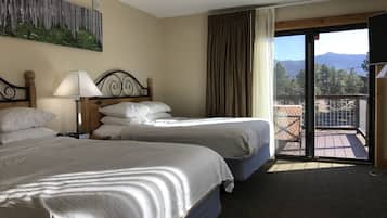 Una camera d'albergo con due letti, un quadro appeso al muro, una lampada e vista sulle montagne dalla finestra.