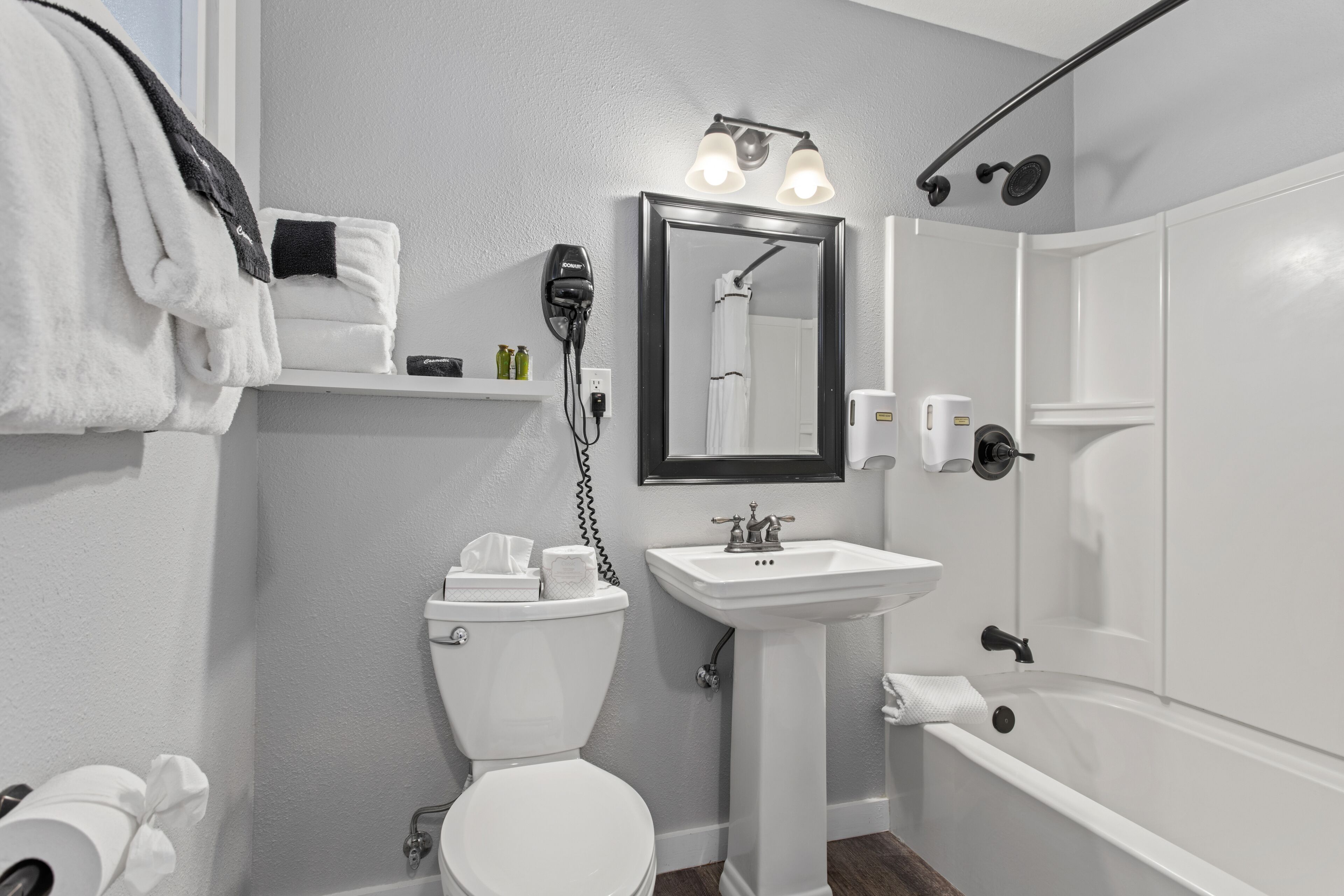 Une salle de bain moderne avec des toilettes, un lavabo et une baignoire. Des serviettes et des articles de toilette sont disposés sur les étagères.