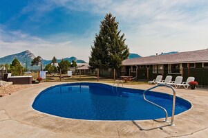A swimming pool with a metal ladder, surrounded by a fence, with lounge chairs and a building in the background.