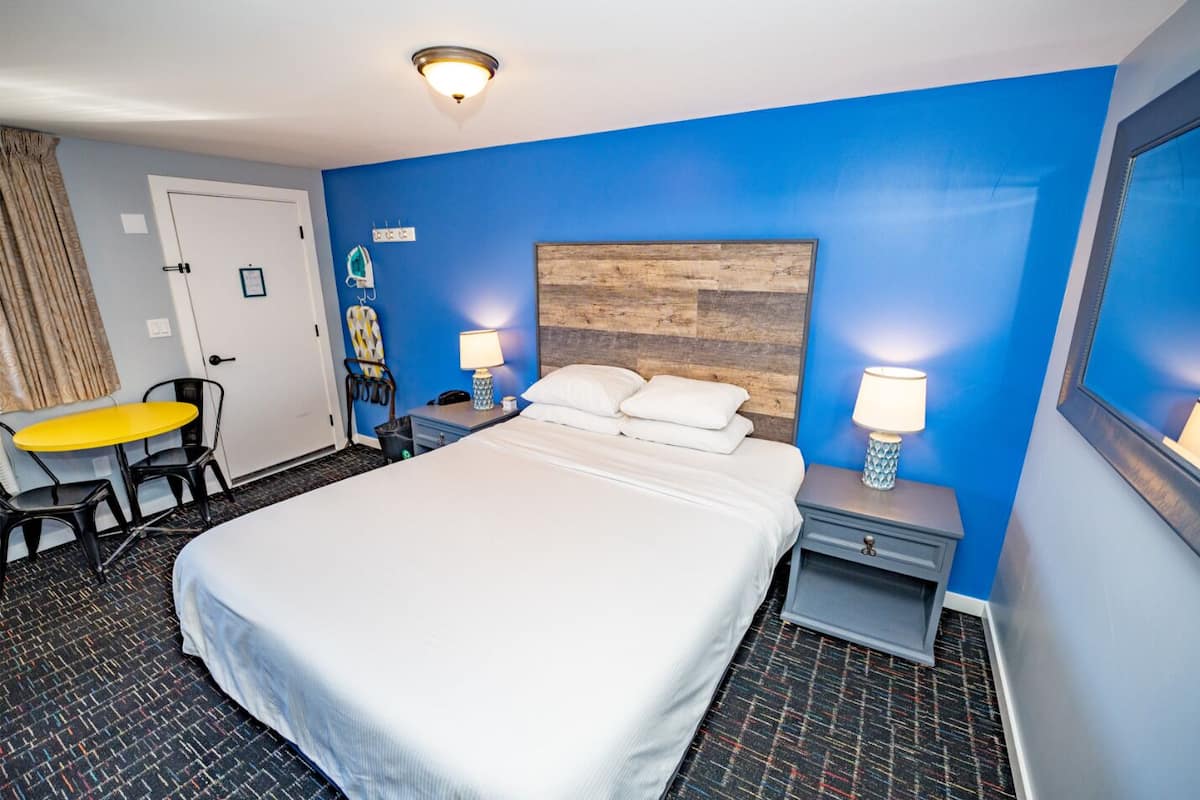 Habitación de hotel con una cama grande, dos mesitas de noche con lámparas, un escritorio con una silla y una pared azul decorativa.