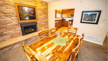 Un coin repas avec une table et des chaises en bois, une cheminée et une cuisine en arrière-plan.