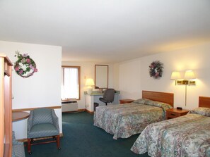 A hotel room with two beds, a desk, a chair, and a desk lamp.