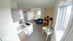 Un espacio habitable compacto con kitchenette, zona de comedor, sofá y una pequeña mesa con objetos.