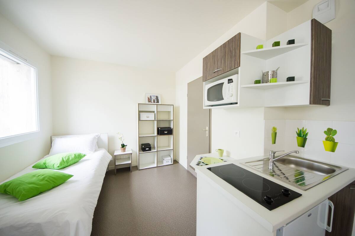 A compact hotel room with a bed, a small kitchenette, a microwave, and a sink.
